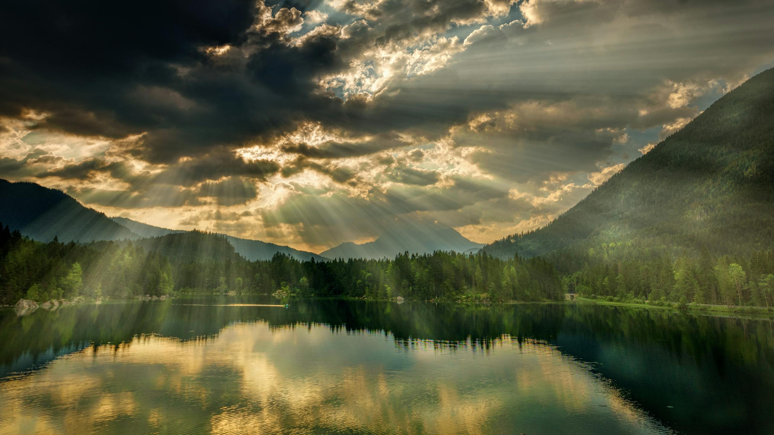 A stunning view of a tranquil lake surrounded by mountains with sunrays piercing through clouds.